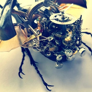 May include: A detailed steampunk-style sculpture of a beetle with intricate gears and clockwork mechanisms. The sculpture is made of metal and has a dark brown and gold finish.