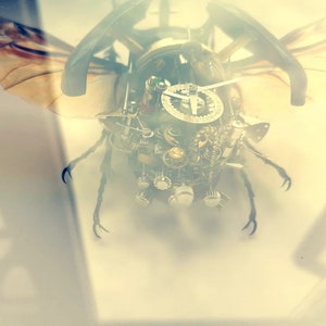 May include: A steampunk-style beetle sculpture made of metal gears and clock parts. The beetle has wings and legs, and its body is covered in intricate details.