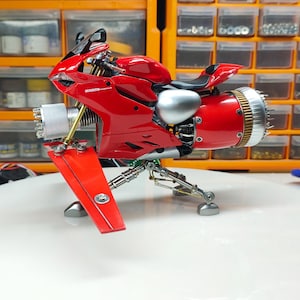 Może przedstawiać: Czerwono-srebrny model motocykla z detalicznym silnikiem i unikalnym designem. Motocykl stoi na białym tle i ma srebrny wydech.
