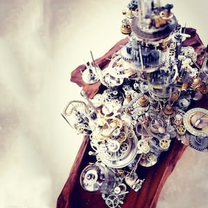 以下が含まれることがあります： 金属製の歯車と時計部品で作られた、精巧なスチームパンク風の彫刻。彫刻は木の板に載せられており、さまざまな複雑なディテールが施されています。