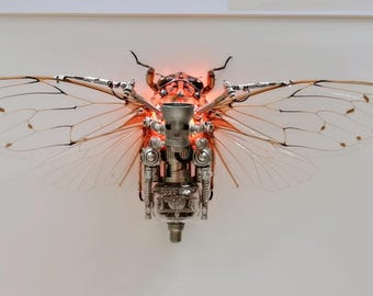 May include: A detailed, metallic sculpture of a cicada with translucent wings. The sculpture is illuminated from within, creating a warm, orange glow.
