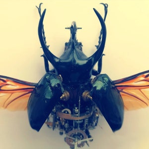 May include: A black and green beetle with orange wings, made of metal gears and clockwork. The beetle is posed with its wings spread out.