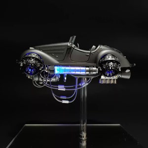 May include: A black, vintage-style car with a futuristic design, featuring glowing blue lights and intricate details. The car is mounted on a clear stand, showcasing its unique features.