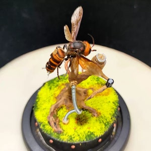May include: A detailed, handcrafted model of a hornet perched on a branch with a steampunk aesthetic. The hornet is made of metal and resin, with intricate details and a realistic appearance. The branch is made of wood and metal, and is decorated with gears and other steampunk elements.