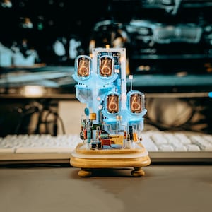 May include: A clock made of clear plastic with four Nixie tubes displaying the numbers 6, 6, 6, and 6. The clock is on a wooden base with a gold finish.