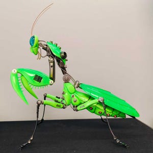 May include: A detailed sculpture of a robotic praying mantis. The insect is primarily bright green with metallic silver and black accents. The sculpture features intricate mechanical details, including articulated legs, wings, and head.