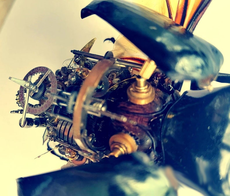 May include: A close-up of a steampunk-style insect sculpture with intricate gears and mechanisms. The sculpture is made of metal and has a dark blue and brown color scheme.