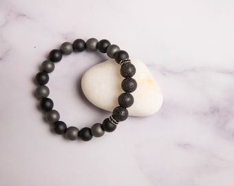 Peut inclure: Un bracelet en perles noires et grises avec un accent argenté. Le bracelet est sur une surface en marbre blanc.