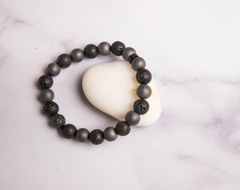 Peut inclure: Un bracelet en perles noires et grises avec une pierre blanche en arrière-plan.