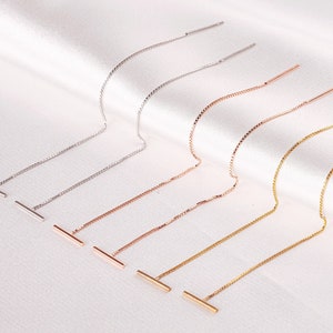 May include: Five pairs of delicate chain earrings with a bar pendant. The earrings are available in silver, rose gold, and gold.