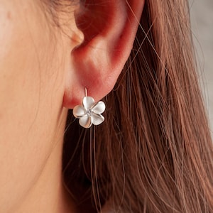 May include: Silver flower earrings with a small clear stone in the center. The earrings are in the shape of a plumeria flower.