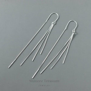 May include: Silver dangle earrings with a chain and three thin strands hanging down. The earrings are from Shineez Treasure Jewelry.