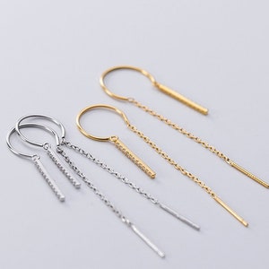 May include: Two pairs of dangle earrings with a small hoop and a long chain with a bar pendant. One pair is gold and the other is silver.