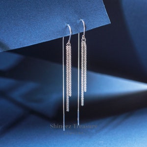 May include: A pair of silver dangle earrings with a delicate chain design. The earrings are hanging from a blue background.