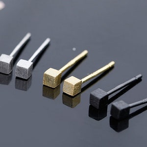 May include: Four pairs of minimalist earrings with square-shaped studs in silver, gold, and black.