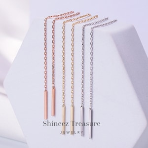 May include: Five pairs of long, thin, dangling earrings with a small bar at the end. The earrings are in different colors: rose gold, gold, silver, and white gold.