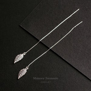 May include: A pair of silver dangle earrings with leaf-shaped charms hanging from thin chains. The earrings are displayed against a black background.