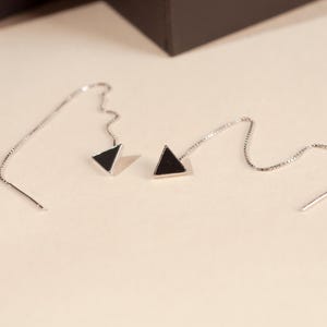 May include: A pair of silver dangle earrings with black triangle charms hanging from delicate chains.