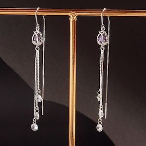 May include: A pair of silver dangle earrings with a purple gemstone at the top and three smaller clear gemstones dangling below.