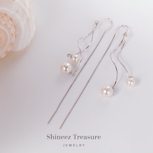 May include: A pair of silver dangle earrings with a pearl and a small diamond accent. The earrings have a long, thin chain that hangs down from the pearl.