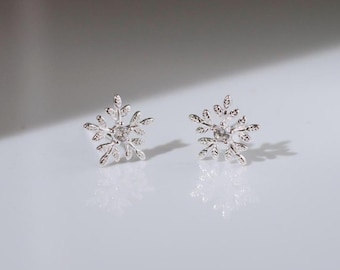 May include: A pair of silver snowflake earrings with a small clear rhinestone in the center of each snowflake.