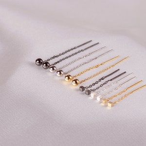 May include: A set of eight delicate earrings featuring a variety of chain styles and finishes. The earrings have either a small ball or a cube charm at the end.