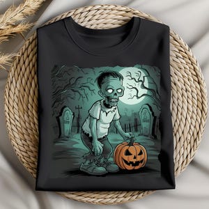 Könnte beinhalten: Schwarzes T-Shirt mit Rundhalsausschnitt und Halloween-Motiv. Das Design zeigt einen grünen Zombie, der einen orangefarbenen geschnitzten Kürbis in einem Friedhof hält, mit einem Vollmond im Hintergrund.