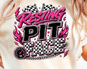 Puede incluir: Camiseta color crema con un diseño gráfico. El diseño presenta las palabras "Resting Pit Face" en rosa y negro, junto con banderas a cuadros, llamas y un velocímetro. La camiseta tiene mangas cortas.