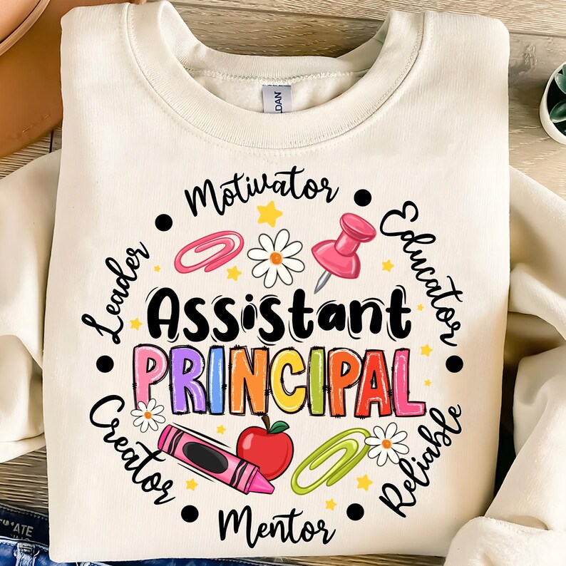 May include: Cream-colored sweatshirt with the words "Assistant Principal" in colorful letters. The design includes a push pin, paper clips, a crayon, an apple, and the words "Motivator", "Leader", "Creator", "Mentor", "Reliable", and "Educator".