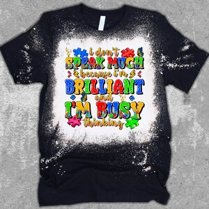May include: Black t-shirt with a white bleach design. The design features a colorful puzzle piece pattern and the text "I don't speak much because I'm brilliant and I'm busy thinking."