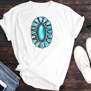 May include: White t-shirt featuring a turquoise and silver turquoise-style design.