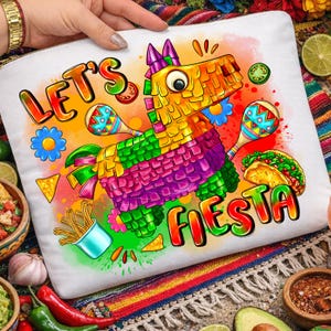 Op de afbeelding: Witte etui met ritssluiting met een kleurrijk "Let's Fiesta"-ontwerp. Het ontwerp toont een piñata, maracas, een taco en andere feestelijke elementen. De etui wordt door een persoon vastgehouden.