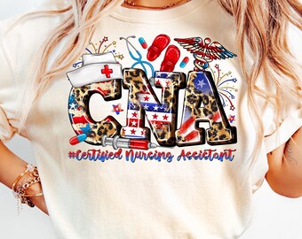 Op de afbeelding: Crèmekleurig T-shirt met de letters "CNA" in een patriottisch ontwerp met luipaardprint accenten. Het shirt bevat medische thema-afbeeldingen zoals een stethoscoop, pillen en een spuit, met de tekst "#Certified Nursing Assistant".