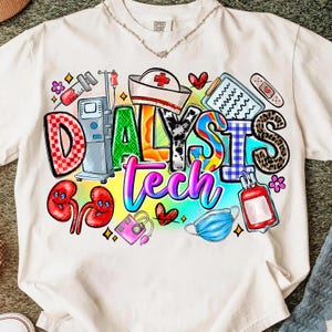 Puede incluir: Camiseta blanca con un diseño gráfico colorido. El diseño incluye las palabras "DIALYSIS Tech" con ilustraciones médicas como un gorro de enfermera, riñones y equipos médicos. La camiseta tiene cuello redondo y mangas cortas.