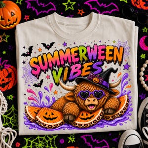 May include: A beige t-shirt featuring a graphic of a brown highland cow wearing a black witch hat and purple heart-shaped sunglasses. The cow rests among orange jack-o'-lantern slices and purple liquid. Text reads SUMMERWEEN VIBES.