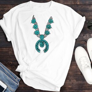 May include: White t-shirt featuring a turquoise and silver necklace design. The necklace has a large pendant with a turquoise stone and silver accents.