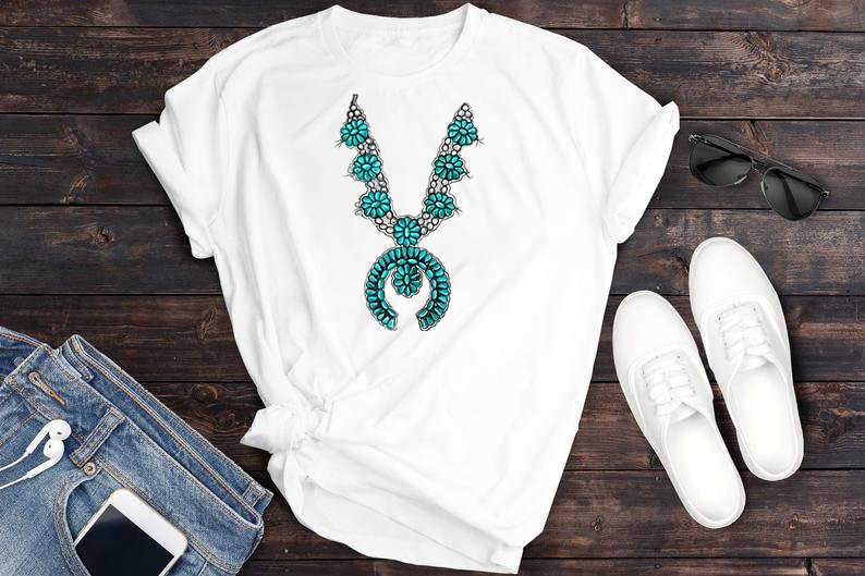 May include: White t-shirt featuring a turquoise and silver necklace design. The necklace has a large pendant with a turquoise stone and silver accents.