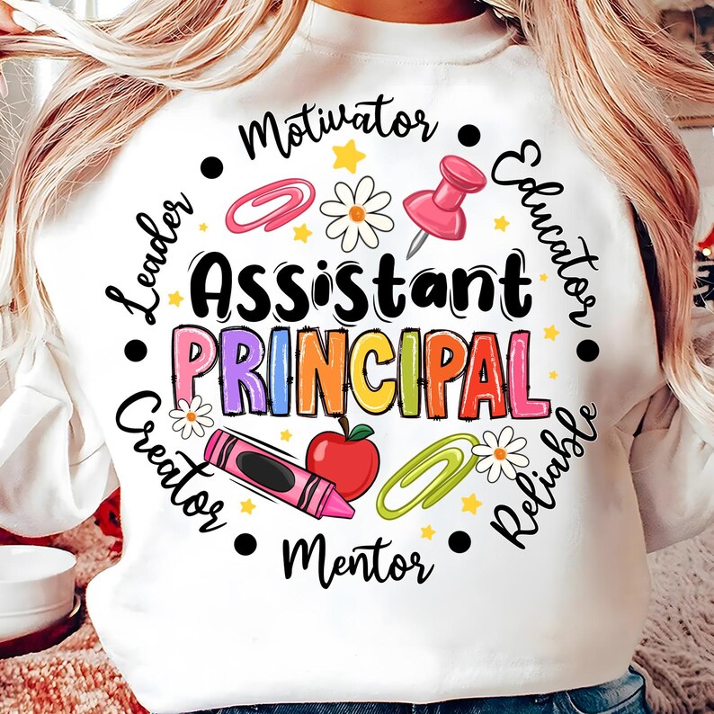 May include: White sweatshirt with the words "Assistant Principal" in colorful letters. The design includes a red apple, a pink push pin, a crayon, and other school-themed graphics. The words "Motivator", "Leader", "Creator", "Mentor", "Reliable", and "Educator" are also included.