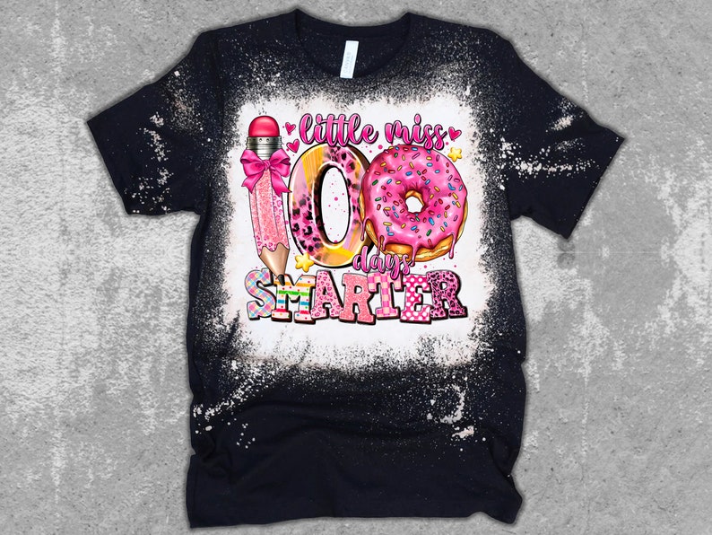 May include: A black t-shirt with a bleach-splattered design featuring a pink pencil, a donut, and the text "little miss 100 days smarter".