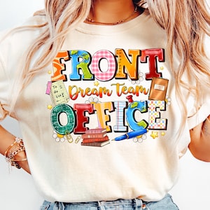 以下が含まれることがあります： クリーム色のTシャツ。カラフルなブロック体で「FRONT Dream Team OFFICE」と書かれています。デザインには地球儀、本、ペン、その他のオフィスをテーマにしたグラフィックが含まれています。Tシャツはクルーネックで半袖です。