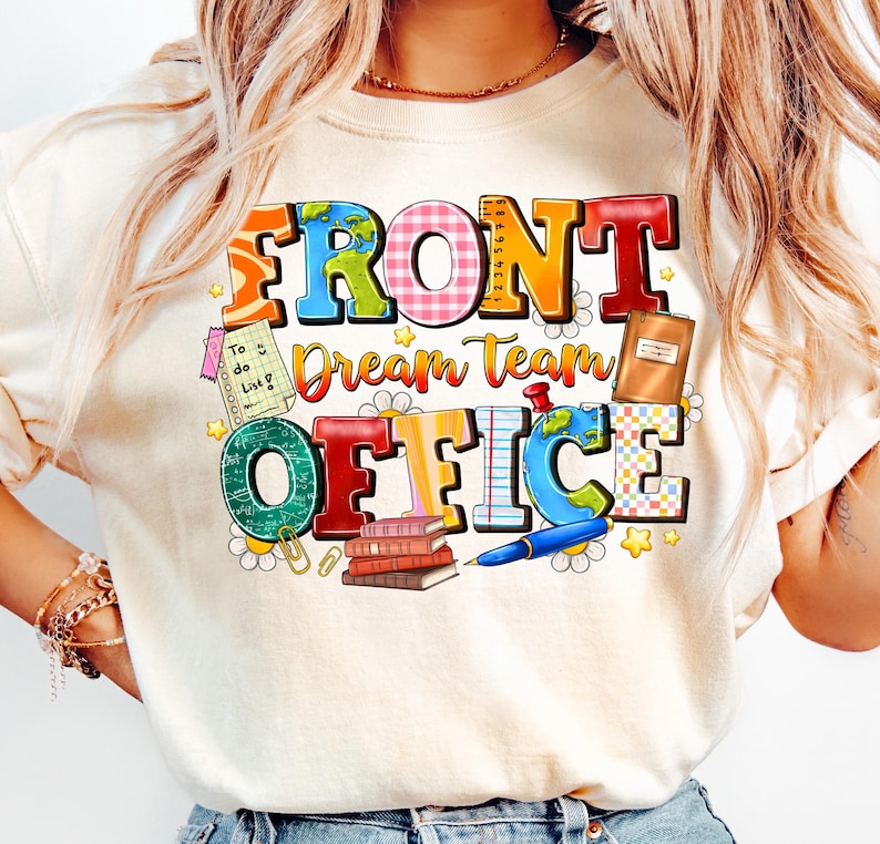 以下が含まれることがあります： クリーム色のTシャツ。カラフルなブロック体で「FRONT Dream Team OFFICE」と書かれています。デザインには地球儀、本、ペン、その他のオフィスをテーマにしたグラフィックが含まれています。Tシャツはクルーネックで半袖です。