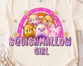 Puede incluir: Camiseta color crema con un gráfico colorido. El diseño incluye un arcoíris, margaritas y varios personajes de animales de dibujos animados. El texto "SQUISHMALLOW GIRL" se muestra en una fuente lúdica.