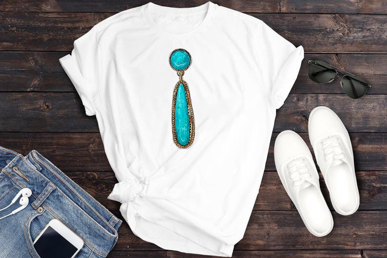May include: A white t-shirt featuring a turquoise gemstone earring pendant. The earring is a teardrop shape with a round stone at the top. The t-shirt is displayed on a wooden surface.
