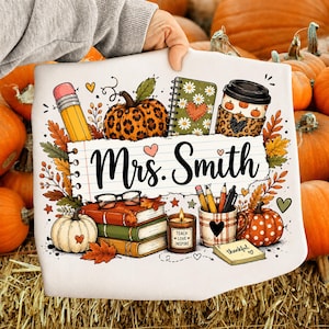 May include: A white t-shirt featuring a graphic print of a leopard-print pumpkin, a notebook, a coffee cup, a stack of books, a candle labeled 'Teach Love Inspire', and a pencil holder. The text 'Mrs. Smith' is centered on a lined paper design.