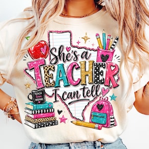 Può includere: Una t-shirt color crema con una grafica dello stato del Texas riempita di carta a righe. Il testo recita She's a Teacher I can tell. Il design include una mela rossa, un portamatite rosa, una pila di libri, uno zaino rosa e matite.