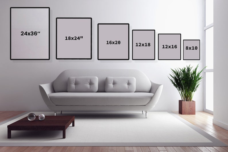 Puede incluir: Un sof&aacute; blanco con dos almohadas se encuentra frente a una pared blanca con seis cuadros negros enmarcados. Los cuadros est&aacute;n etiquetados con sus dimensiones en pulgadas: 24x36, 18x24, 16x20, 12x18, 12x16 y 8x10. Una mesa de caf&eacute; de color marr&oacute;n oscuro se encuentra frente al sof&aacute; con dos orbes de vidrio transparentes en la parte superior.