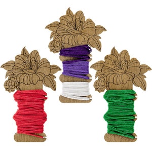 May include: Three wooden thread holders with floral designs. Each holder has a different color of thread wound around it: red, white and purple, and green.