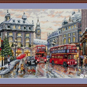 May include: A snowy London street scene with red double-decker buses, a clock tower, and people walking. The scene is lit up with Christmas lights and there is a red umbrella in the foreground.