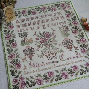 Peut inclure: Une broderie au point de croix vintage avec un alphabet, des chiffres et des motifs floraux. Le motif comprend des roses, des oiseaux et un cygne, avec l'année 1896. La bordure est verte, et les couleurs sont des roses et des verts sourds.