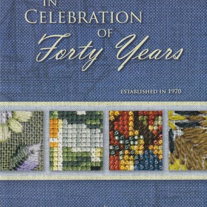 May include: A blue fabric with the text "IN CELEBRATION OF Forty Years" and "ESTABLISHED IN 1970". Four small, square cross-stitch designs are displayed below the text, with a logo at the bottom.
